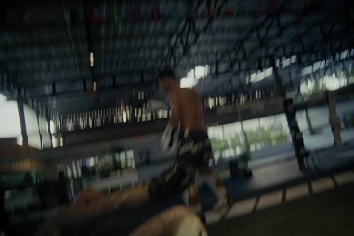 A slow-motion, low-angle shot shows a tattooed Muay Thai fighter getting knocked down by a kick before slowly rising back to his feet with a smile