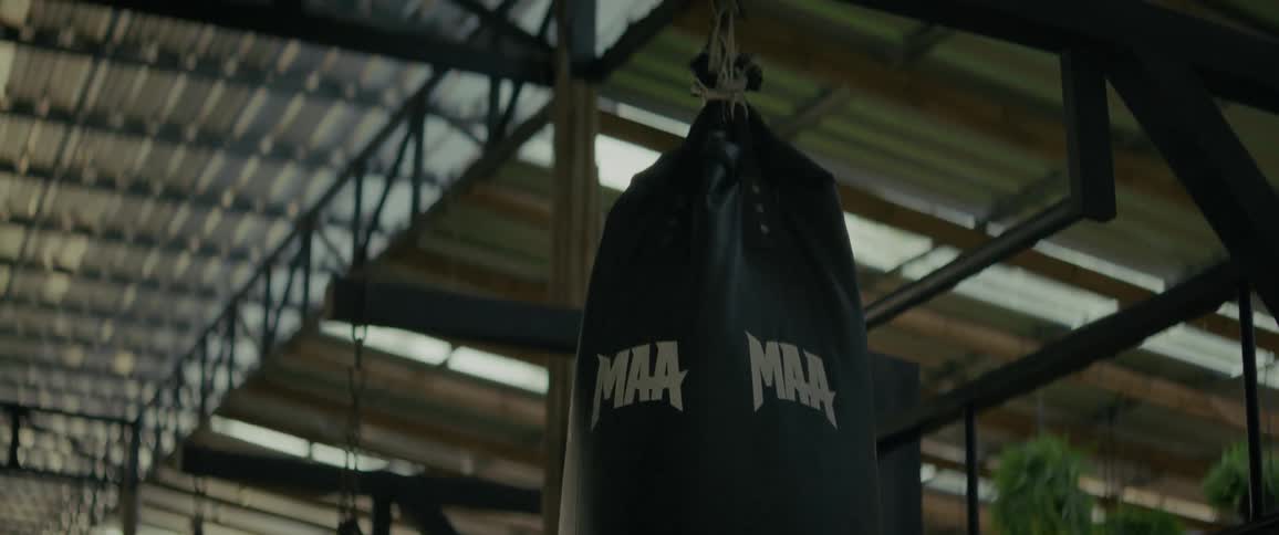 A slow-motion close-up shot pans up on a black MMA punching bag hanging in a gym
