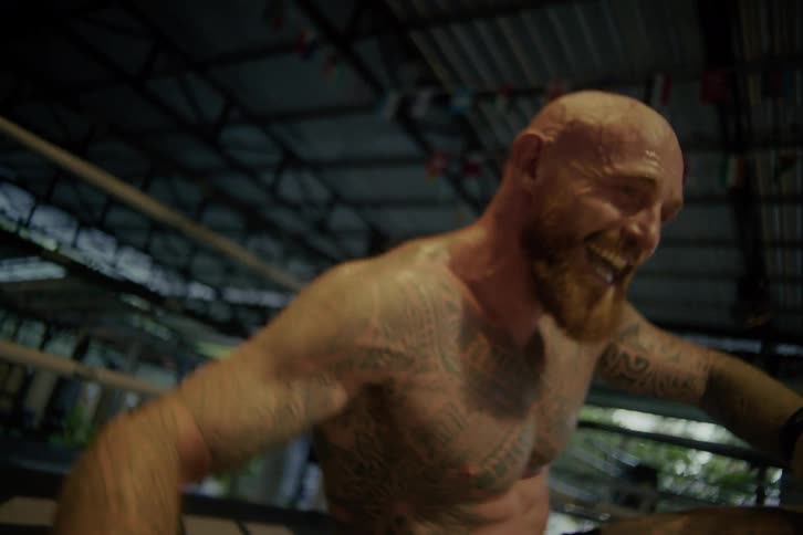 A resilient tattooed boxer smiles through the pain as he pushes himself up from the ring floor in dramatic slow motion