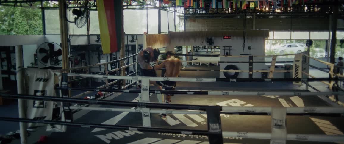 Two muscular men spar in a kickboxing ring, with one delivering a knockout blow to the other in a dramatic slow-motion sequence