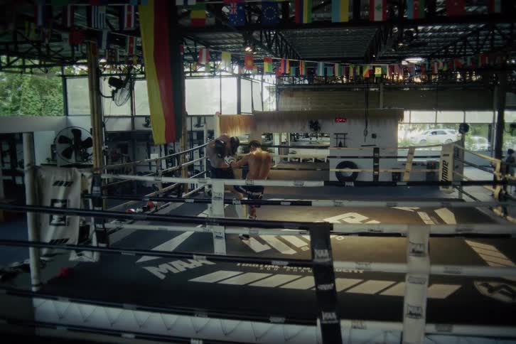 Two male Muay Thai fighters spar in a boxing ring, with one delivering a decisive knockout blow to the other