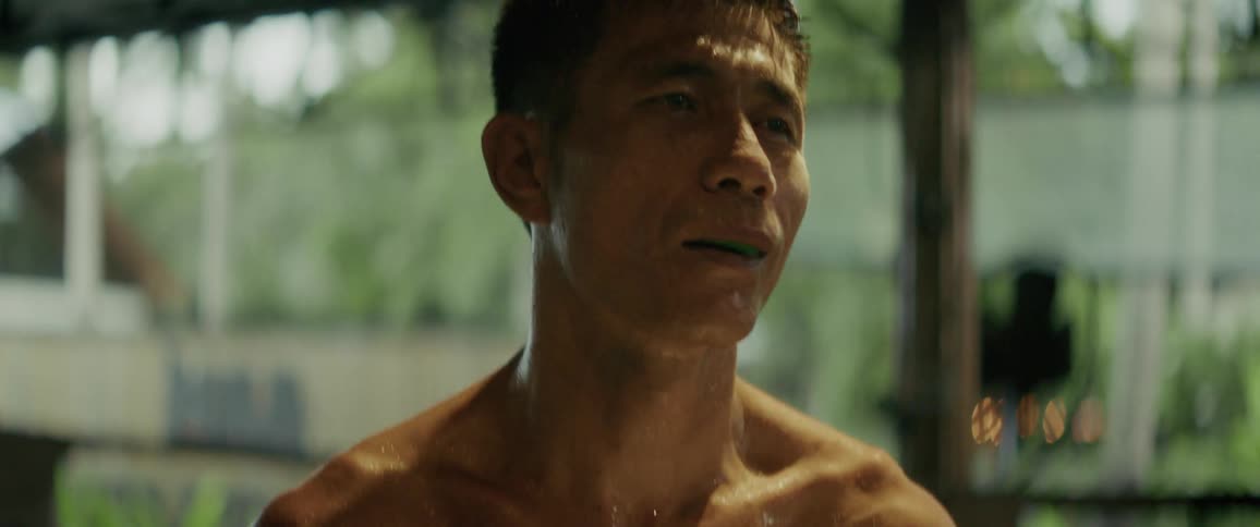 A sweaty and determined boxer with a mouthguard trains in slow motion in an outdoor ring