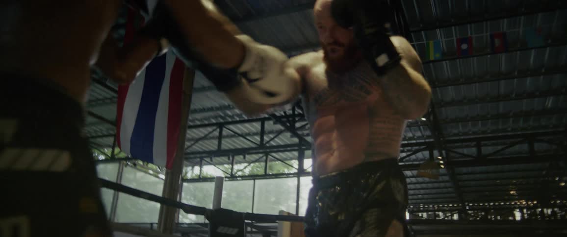 Two powerful Muay Thai fighters trade intense blows and kicks in a gritty, backlit boxing ring during a slow-motion sparring session