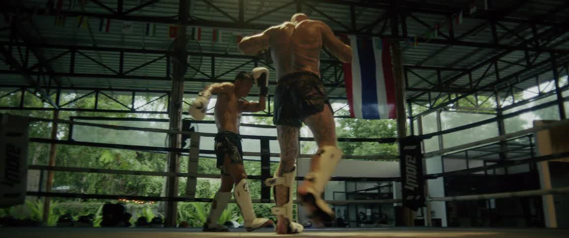 Two muscular Muay Thai fighters spar intensely in a boxing ring, filmed in dramatic slow motion