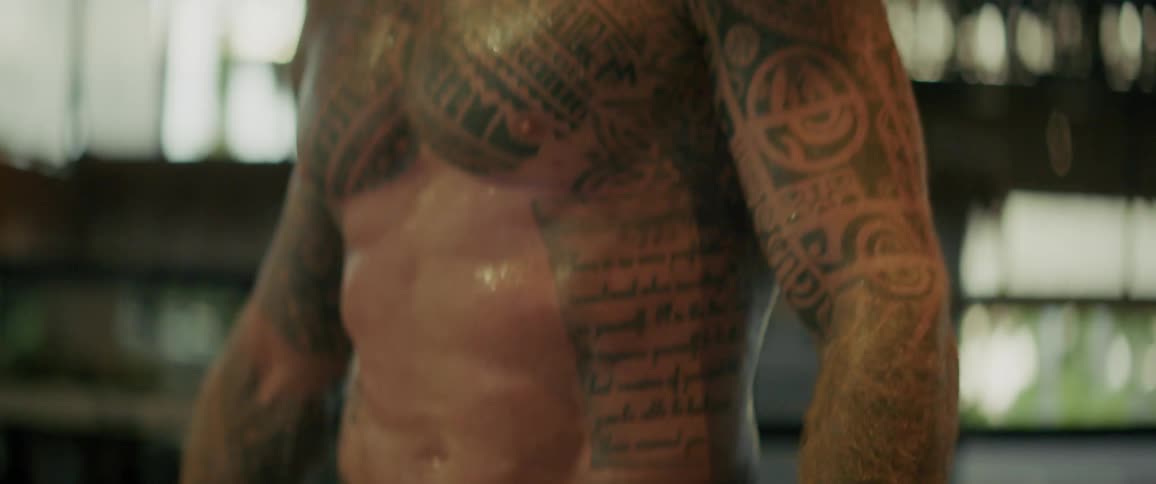 Tight shot of a powerful, tattooed athlete's defined abs and muscular torso during an intense workout