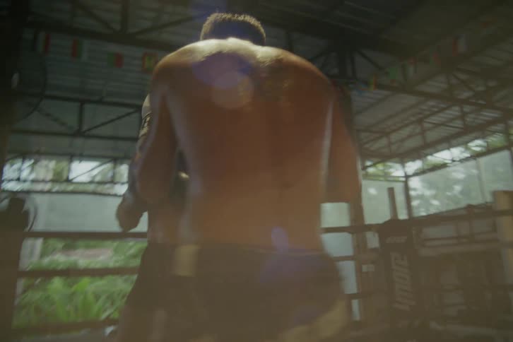 Intense slow-motion sparring session between two powerful Muay Thai fighters in a gritty, open-air boxing ring
