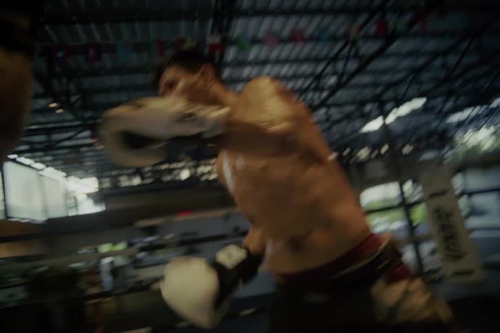In a gritty boxing ring, two Muay Thai fighters exchange powerful blows in slow motion until one is knocked out by a devastating kick