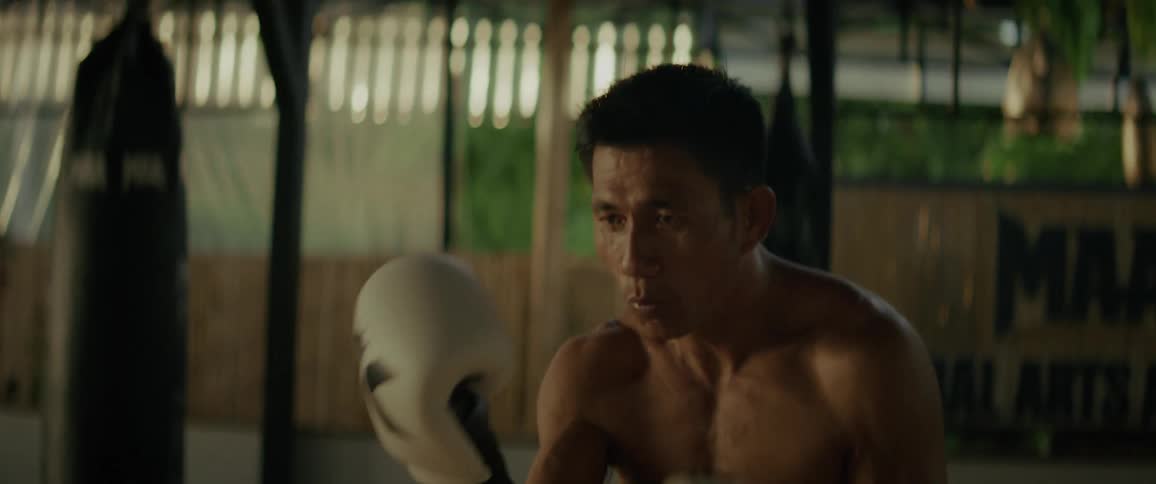 Slow-motion close-up of a shirtless Asian boxer training intensely and throwing punches in an open-air gym