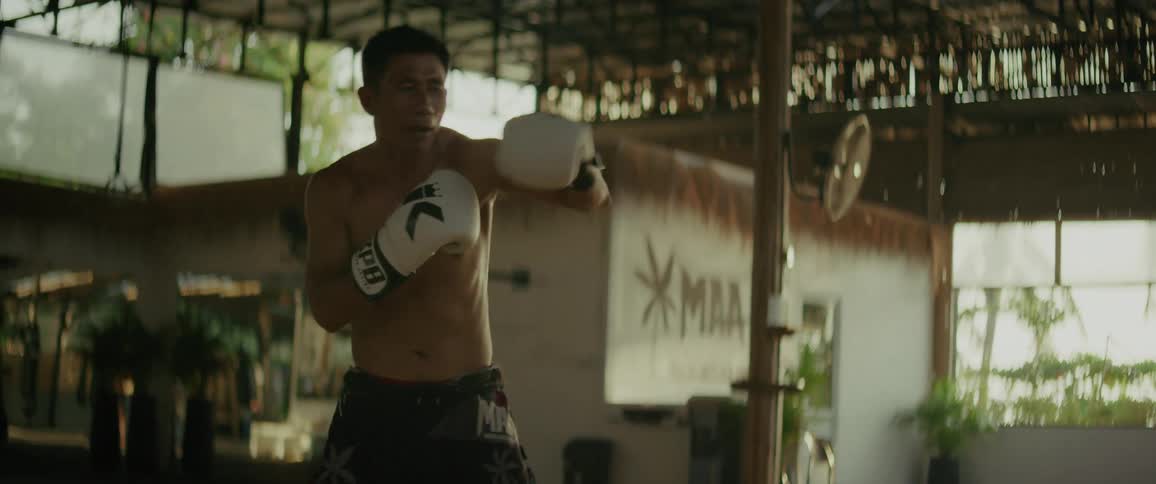A focused male fighter practices his punches in slow motion at a rustic, open-air MMA gym
