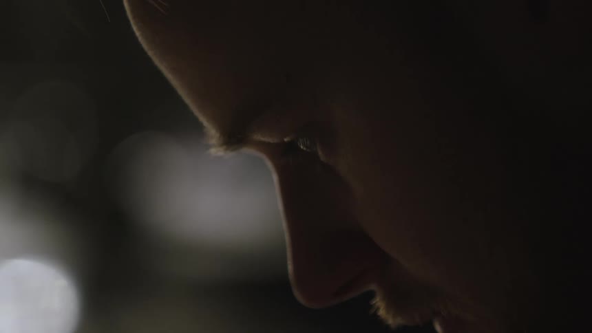 An extreme close-up profile shot of a contemplative man's face as he looks down in the dark