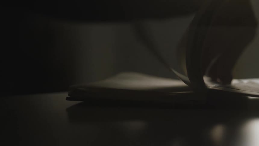 A hand quickly flips through the pages of a book in a dark, dimly lit room