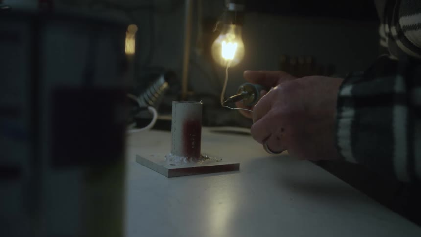 Close-up of hands using a soldering iron to carefully connect wires in a dimly lit workshop