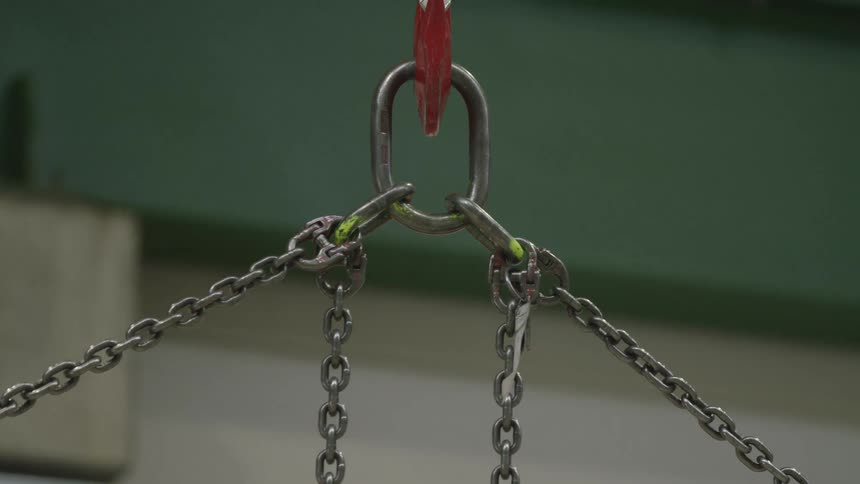 A close-up of a heavy-duty industrial chain and hook assembly swaying gently in a factory setting