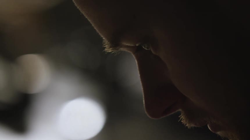 Close-up profile shot of a man's face in shadow as he looks down in deep thought