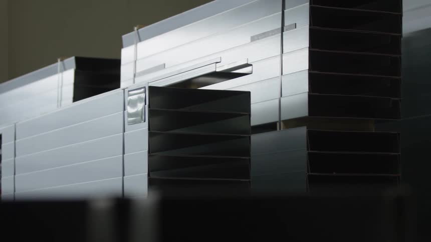 A slow rightward slide reveals stacks of shiny, rectangular metal profiles neatly organized in a warehouse