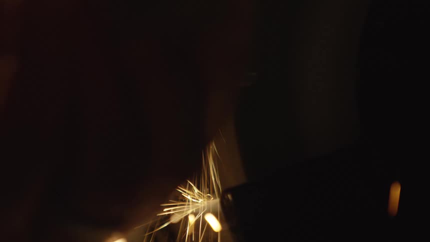 Sparks fly in dramatic slow motion as a metal tool is sharpened on a grinding wheel in a dark setting