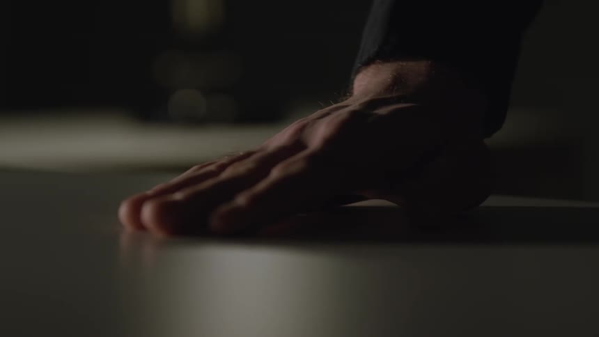 Close-up of a man's hand sliding across a tabletop in a dark and mysterious room