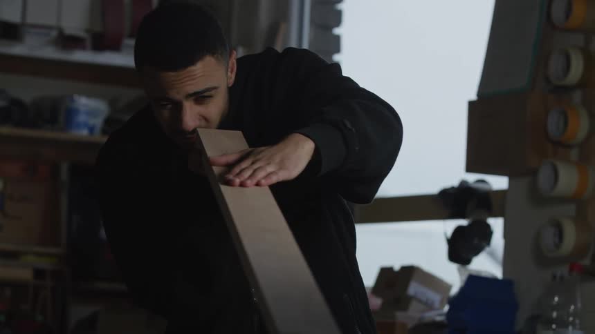 A young woodworker in his workshop carefully inspects a wooden plank for imperfections in slow motion