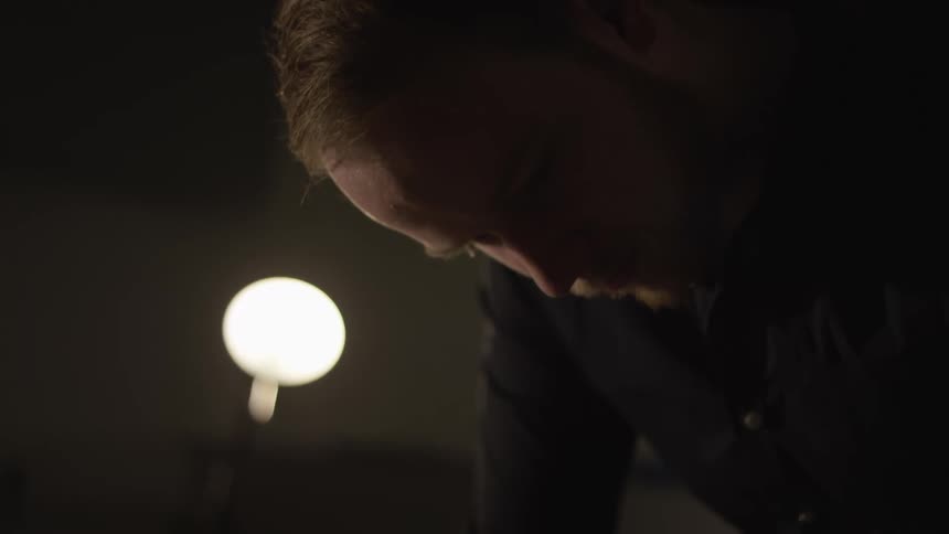 Intimate close-up of a bearded man concentrating intensely in a dimly lit room