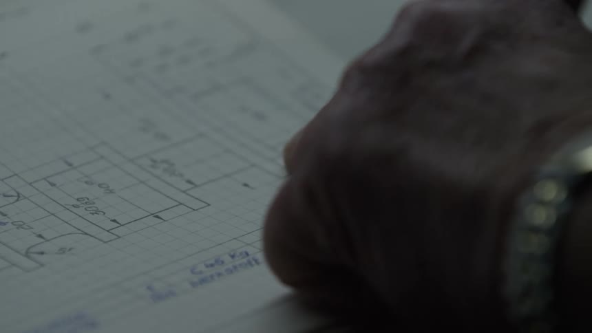 Close-up of a designer's hand tracing the dimensions on a hand-drawn technical schematic