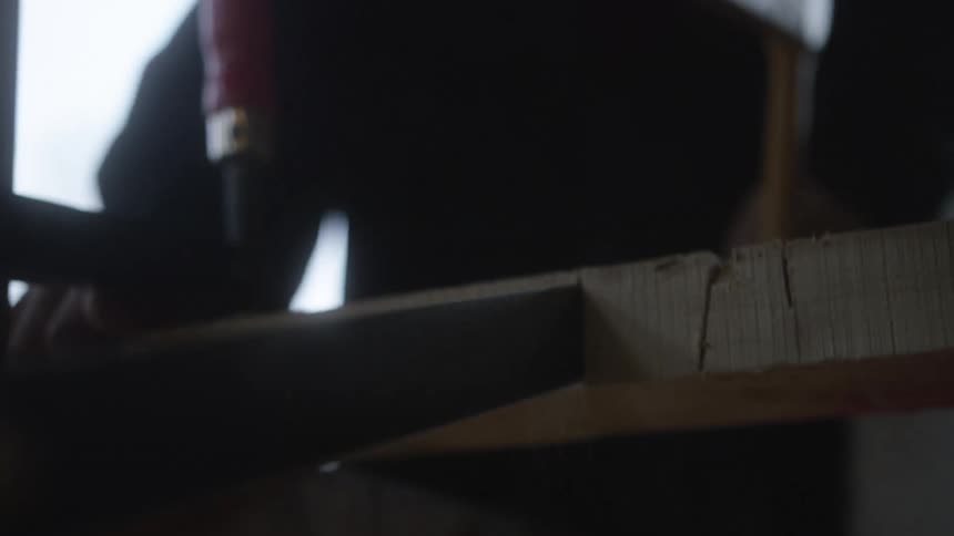 Two woodworkers collaborate in a rustic workshop, one sawing a wooden board while the other uses a chisel and mallet