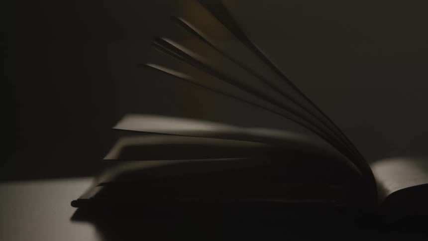 The pages of an open book slowly flip over in a dark and moody setting