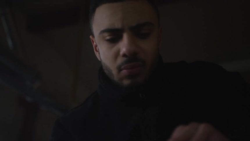 A focused young man carefully sands a piece of wood in slow motion in a dimly lit workshop