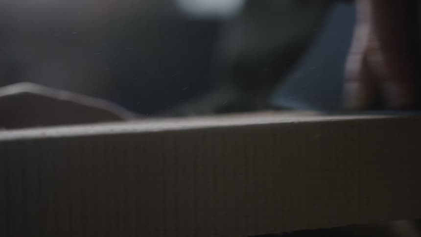 A close-up, slow-motion shot of a hand sanding a piece of wood, with fine sawdust flying into the air