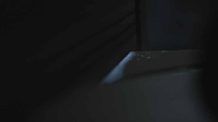 A slow, mysterious pan across a dark, abstract surface reveals a silhouetted hand in a dimly lit room