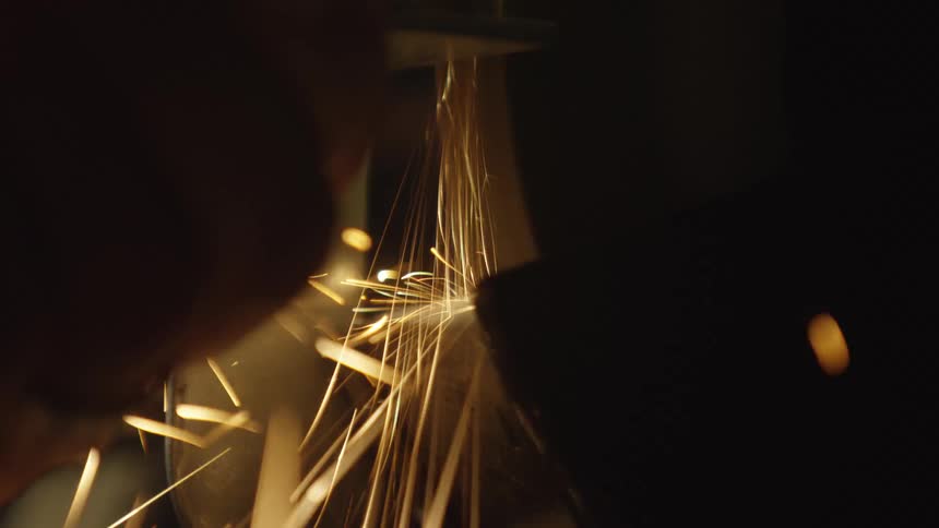A dramatic close-up, slow-motion shot of a metal grinder creating a shower of hot, bright sparks in a dark workshop