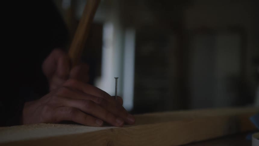 A close-up slow-motion shot of a carpenter repeatedly missing a nail while trying to hammer it into a wooden plank