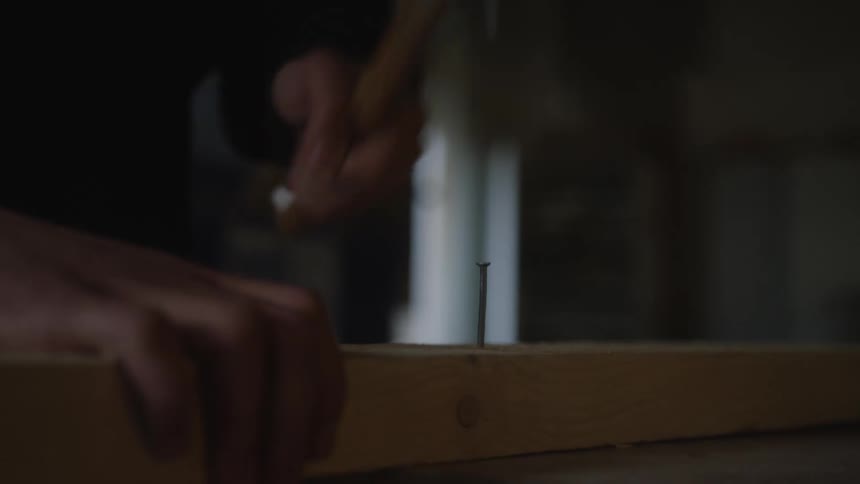 Slow-motion close-up of a person hammering a nail into a wooden plank, ultimately missing a strike and bending it