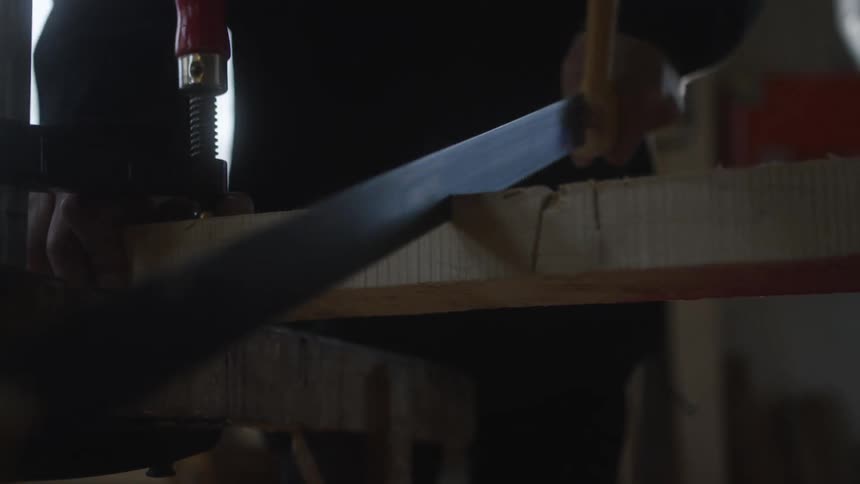 A craftsman carefully saws through a wooden plank clamped to a workbench in a workshop