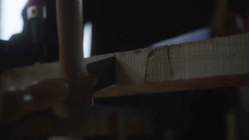 A close-up of a hand saw cutting through a wooden plank in a dimly lit workshop