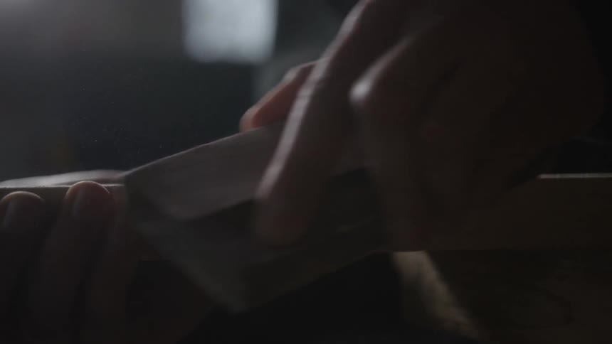 Close-up shot of a carpenter's hands sanding a wooden plank with a sanding block in slow motion