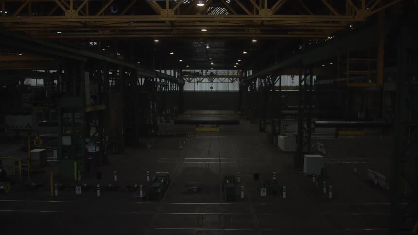 A wide, static shot of a vast and empty industrial warehouse at night