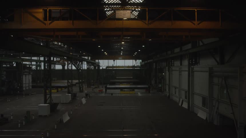 Sparks fly as workers weld large metal pipes inside a vast industrial warehouse