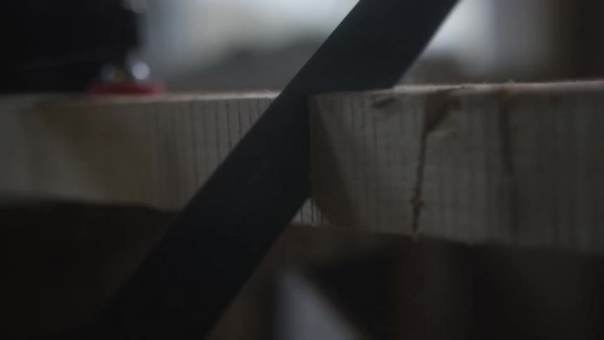Slow-motion close-up of a carpenter meticulously sawing through a wooden plank in a dimly lit workshop