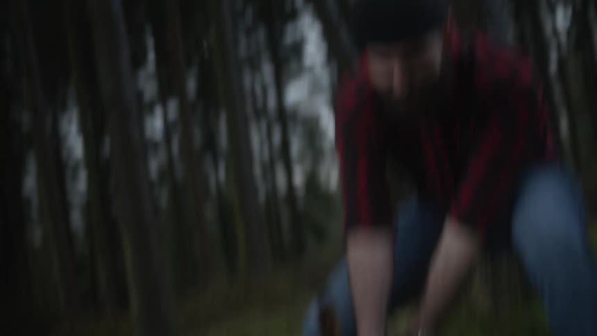 A powerful lumberjack in a red plaid shirt swings his axe in slow motion, forcefully chopping a fallen log in a dense forest