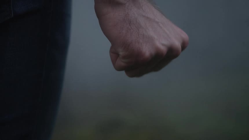 A close-up shot of a man's hand slowly clenching into a tight fist, conveying a sense of anger or tension