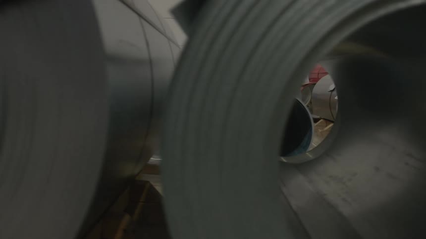 An abstract slow-motion tracking shot moves through the core of a large roll of sheet metal in a factory warehouse