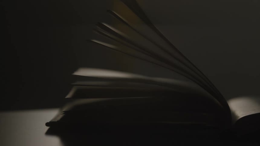 Slow motion shot of pages turning in an open book on a table in the dark