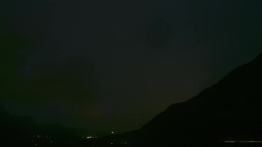 A dramatic nighttime timelapse shows a powerful thunderstorm with frequent lightning strikes over a dark mountain valley