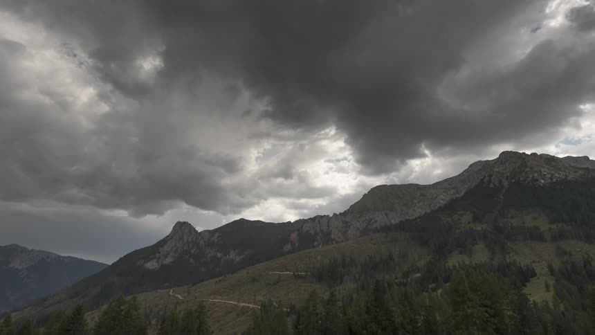 Ominous storm clouds drift over a rugged, forested mountain range
