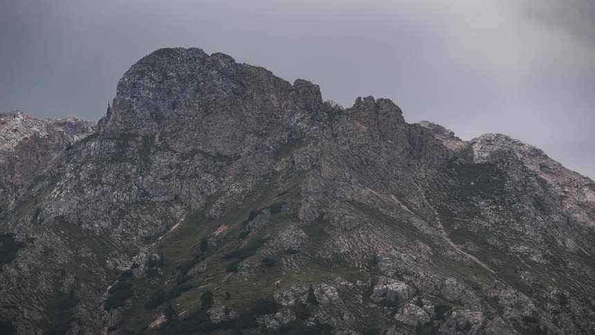 A dramatic timelapse shows dark, ominous clouds swirling over a rugged mountain peak as sunlight breaks through
