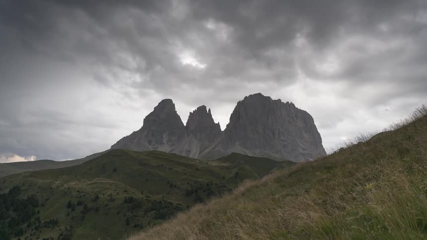 A powerful view of the Sassolungo mountain peaks in the Dolomites stands firm against a backdrop of dark, moving storm clouds