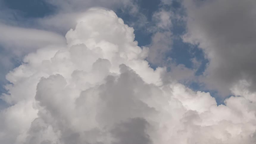 A timelapse of a massive white cumulus cloud billowing and expanding before being overtaken by darker storm clouds