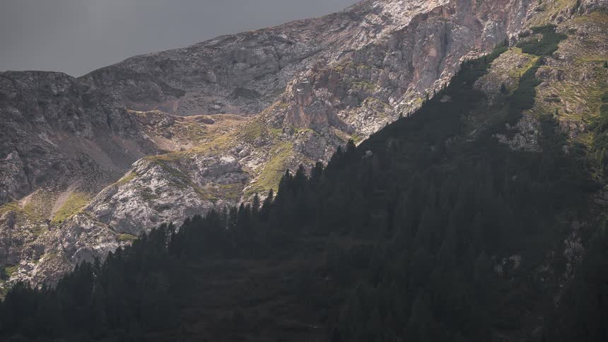 Timelapse of shadows moving across a dramatic rocky mountainside and the dense pine forest below