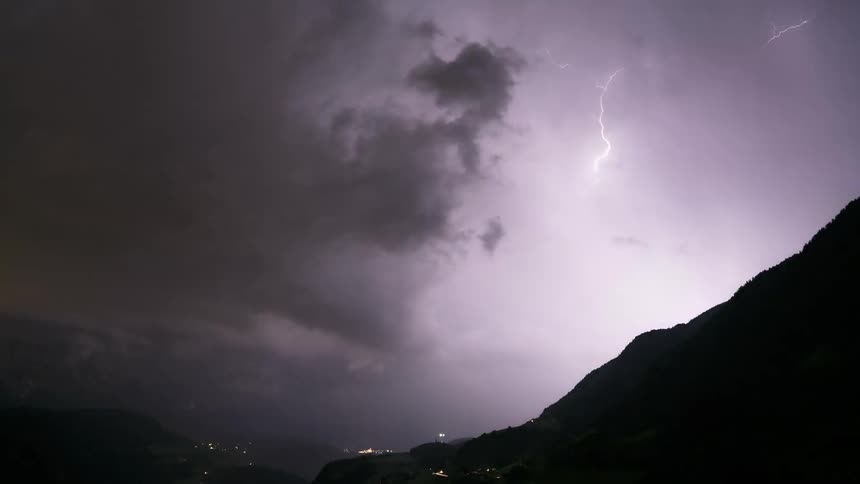 A dramatic time-lapse of a powerful thunderstorm with frequent lightning strikes over a dark mountain valley