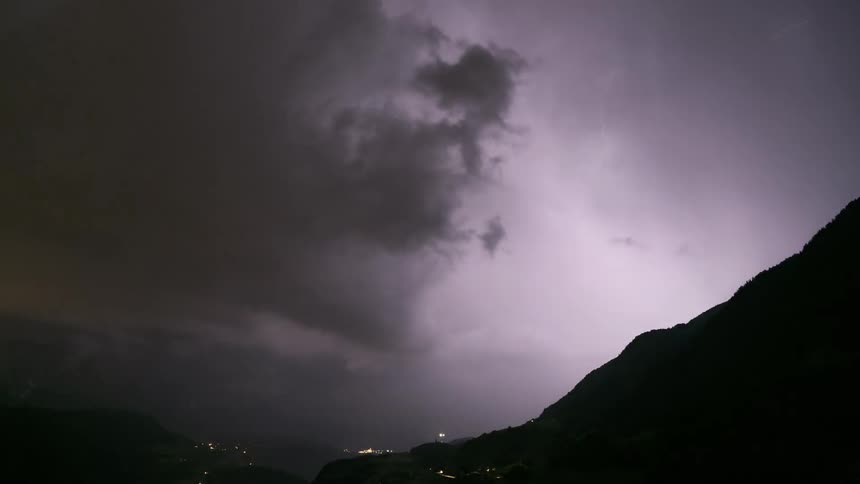 A dramatic timelapse of a powerful lightning storm raging at night over a small town in a mountain valley